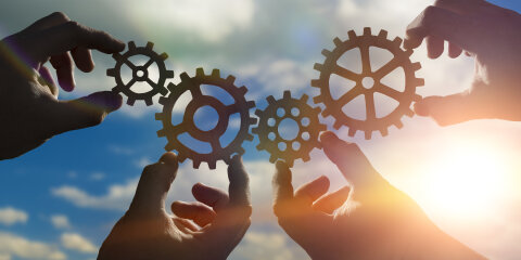 Four hands of businessmen collect from the gears of the details of puzzles. against the background of sunlight. The concept of a business idea. Teamwork. strategy. cooperation