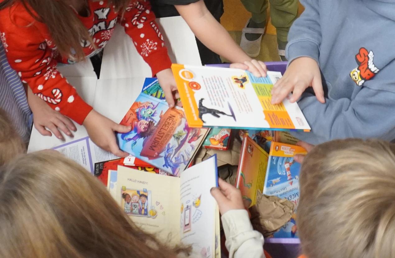 Mehrere Kinder betrachten und halten verschiedene bunte Bücher. Die Szene zeigt Hände, Bücher und teilweise Oberkörper der Kinder.